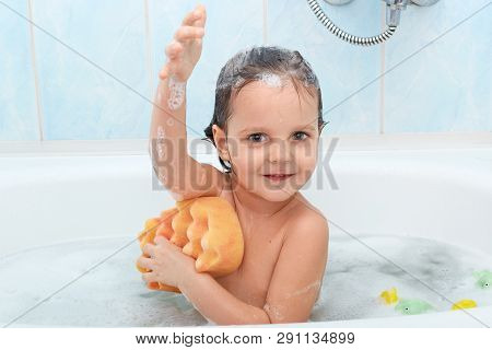 Cheerful Positive Adorable Small Child Taking Bath And Washing Herself With Yellow Sponge, Expresses