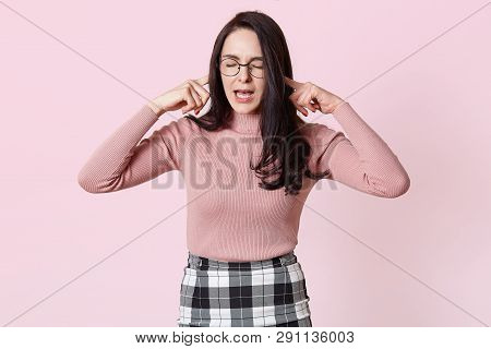 Beautiful Grimacing Young Woman In Pink Sweater, Her Ears With Fingers And She Keeps Eyes Closed. Ch