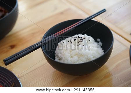 Japanese Rice With Black Sesami On Top In The Black Bowl And Chopsticks On The Wood Table.