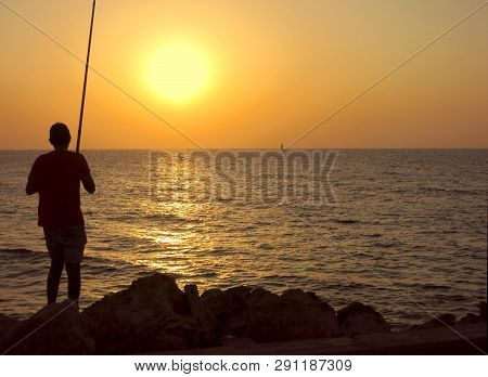 Silhouette Of A Young Man Fishing At The Sea Sunset Background