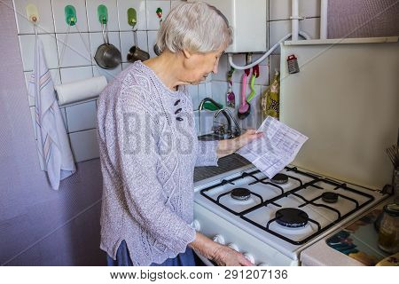 Senior Old Housewife At Home And Examines Gas And Electricity Bills Under Stress When Checking Accou