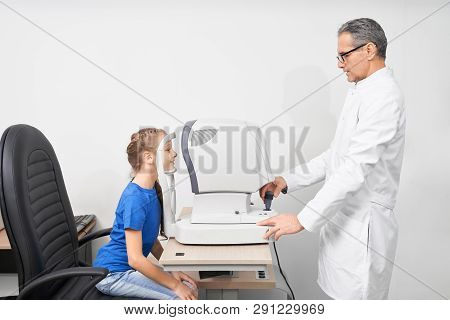 Doctor Optometrist Examining Eyesight Of Young Patient In Optician Office. Eye Specialist In White C