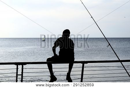 Silhouette Of A Young Man Fishing At A Sea Background