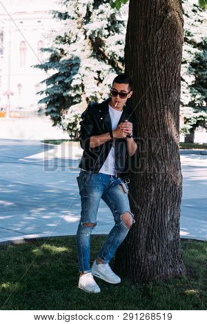 A Young Guy Smokes Around A Tree In The City.bad Habit.smoking In A Public Place