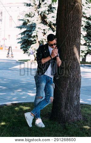 A Young Guy Smokes Around A Tree In The City.bad Habit.smoking In A Public Place