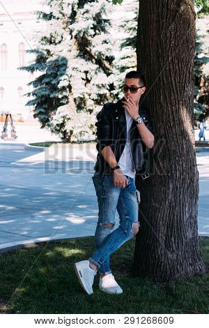 A Young Guy Smokes Around A Tree In The City.bad Habit.smoking In A Public Place
