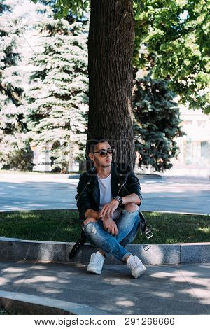 A Young Guy Smokes Around A Tree In The City.bad Habit.smoking In A Public Place