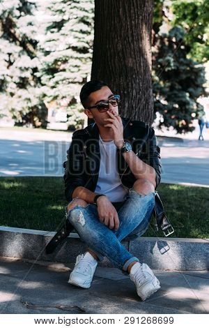A Young Guy Smokes Around A Tree In The City.bad Habit.smoking In A Public Place