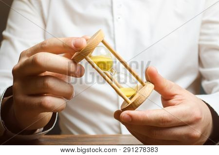 Hourglass In The Hands Of A Businessman In A White Shirt. Planning Time And Reducing Business Costs.