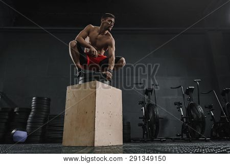 Young Sportive Man Resting After Box Jump Exercise At The Gym. Copy Space