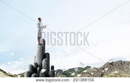 Young Female Doctor With Folder In Hands Satnding On Stone Column