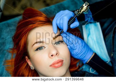 Young Woman Undergoing Procedure Of Permanent Eyebrow Makeup In Tattoo Salon. Beautician Is Doing Pe