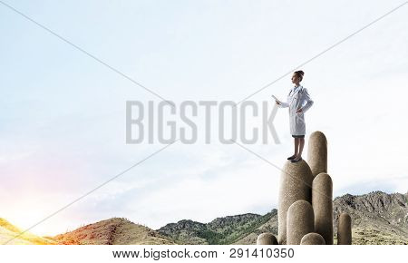 Young Female Doctor With Folder In Hands Satnding On Stone Column