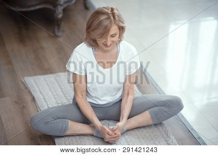 An Elderly Woman Of European Appearance Is Engaged In Yoga. She Conducts Classes At Home. The Woman 
