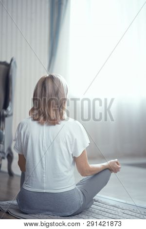 A Woman Is Sitting On The Floor In The Living Room. Looking Out The Window She Is Meditating After Y