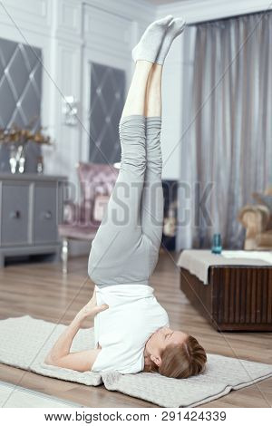 A Woman Over 50 Years Old Enjoys Yoga. She Conducts Classes At Home In The Living Room. Yoga Helps T