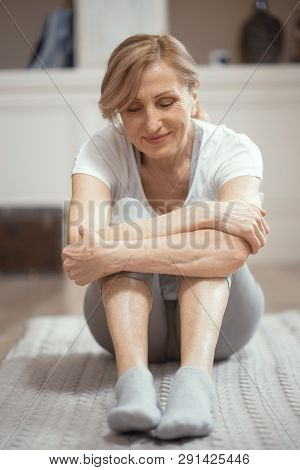Adult Woman Finished Yoga Workout. She Is Engaged At Home In The Living Room. Woman In Good Mood Aft