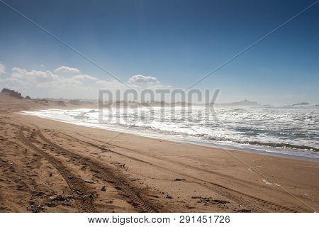 Yellow Sand Of A Beach With A Footprints And Car Tires Imprints. Wild Waves Of The Atlantic Ocean. B