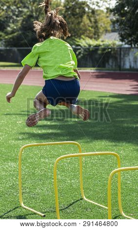 High School Teenage Girl Is Jumping Over A Two Foot Yello Mini Hurdle Spliting Her Feet To The Side 