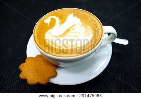 Cappuccino With Swan Drawn On The Foam, In A White Cup With Spoon And Saucer, Black Background