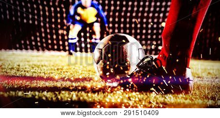 Low section of soccer player with ball against goalkeeper standing on playing field