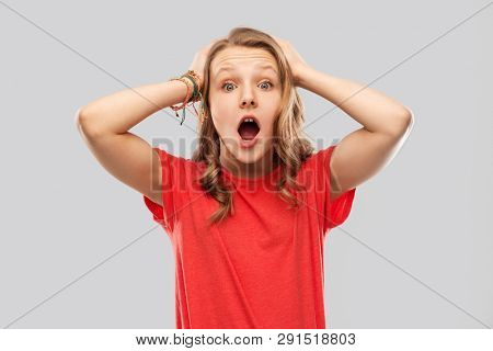 emotion, expression and people concept - impressed or shocked teenage girl with open mouth in red t-shirt over grey background