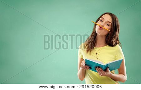 education, school and people concept - teenage student girl in yellow t-shirt with diary or notebook and pencil-mustache over green chalk board background