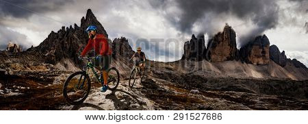 Cycling woman and man riding on bikes in Dolomites mountains andscape. Couple cycling MTB enduro trail track. Outdoor sport activity.