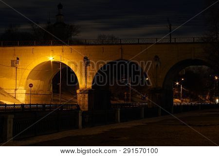 Night City Landscape. Large Stone Arched Bridge Illuminated By A Street Lamp.