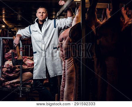 The Butcher In A White Work Shirt Holding Ax While Standing In A Refrigerated Warehouse In The Midst
