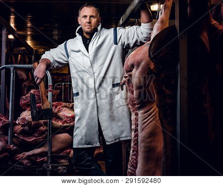 The Butcher In A White Work Shirt Holding Ax While Standing In A Refrigerated Warehouse In The Midst