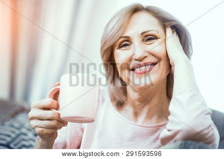 A Woman Over 50 Years Of European Appearance Resting At Home Drinking Coffee. The Woman Smiles Broad