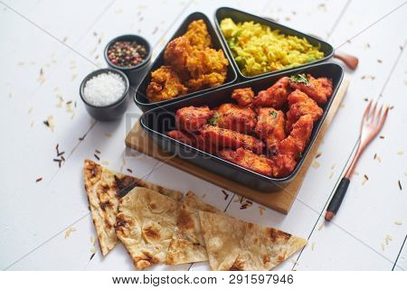 Spicy indian fried chicken served with curry vegetable rice, onion bhajia, naan bread. Placed on white wooden table.