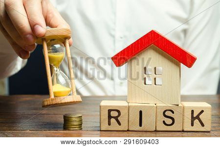 Businessman Holds Clock, Wooden House And The Inscription Risk On Wooden Block. The Concept Of Non-p