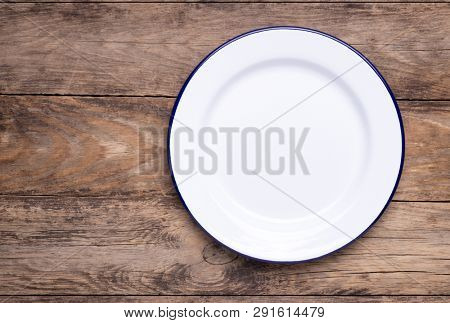 White empty enamel plate on old wooden table, top view