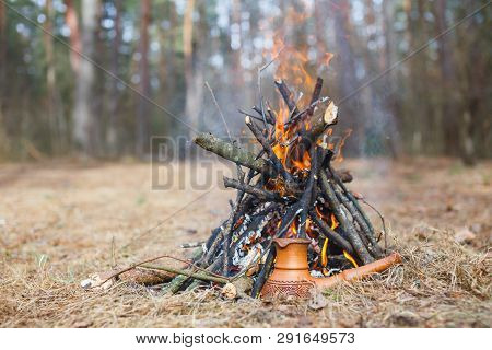 At The Stake In The Spring Forest, A Clay Turkish Coffee Pot Is Heated Against The Grass.