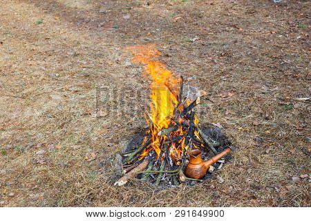 At The Stake In The Spring Forest, A Clay Turkish Coffee Pot Is Heated Against The Grass.