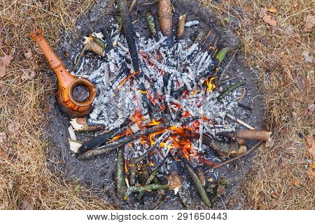 At The Stake In The Spring Forest, A Clay Turkish Coffee Pot Is Heated Against The Grass.