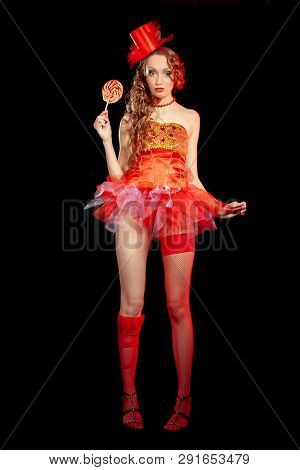 Sexy burlesque dancer stripper posing with sweet lollipop, in red corset and red hat with curly hair