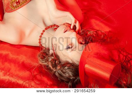 Sexy Burlesque Dancer Stripper Posing With Sweet Lollipop, In Red Corset And Red Hat With Curly Hair