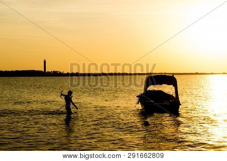 Silhouette Of Man Carrying The Anchor Of Boat Out To Sea