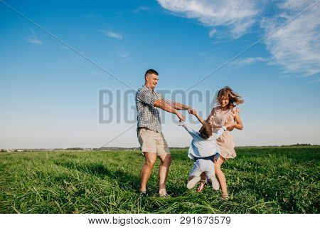 Mother And Father Swinging Son In Sunnny Summer Day