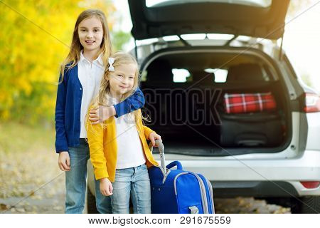 Two Adorable Girls With A Suitcase Going On Vacations With Their Parents. Two Kids Looking Forward F