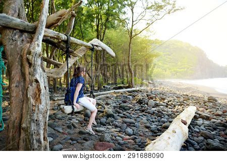 Young Female Tourist Relaxing On A Handmade Swing On Rocky Beach Of Pololu Valley On Big Island Of H
