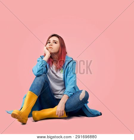 Young Beautiful Girl In Blue Coat And Yellow Rubber Boots Sits With Sad Expression In Her Eyes. She 