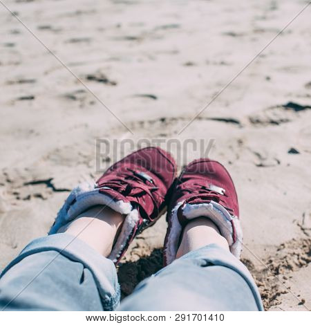 Feet Of Young Woman In Sport Footwear And Jeans Relaxing After Hiking On Sand Beach. Square Pov. Adv