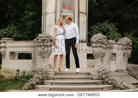 Beautiful Cuple Stand On The Stairs And Hug Each Other. Man And Woman Walking In The Park. Love Stor
