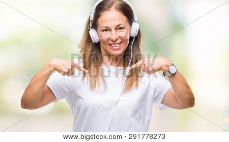 Middle age hispanic woman listening to music wearing headphones over isolated background looking confident with smile on face, pointing oneself with fingers proud and happy.