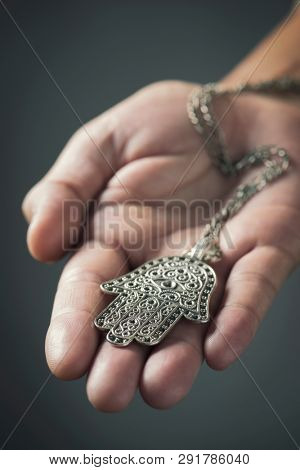 closeup of an old hamsa amulet, also known of the hand of fatima or the hand of mary, on the palm of the hand of a young man