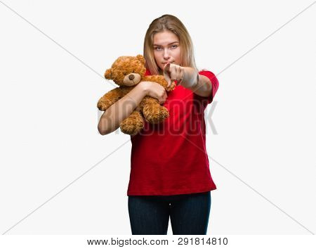Young caucasian woman holding cute teddy bear over isolated background pointing with finger to the camera and to you, hand sign, positive and confident gesture from the front